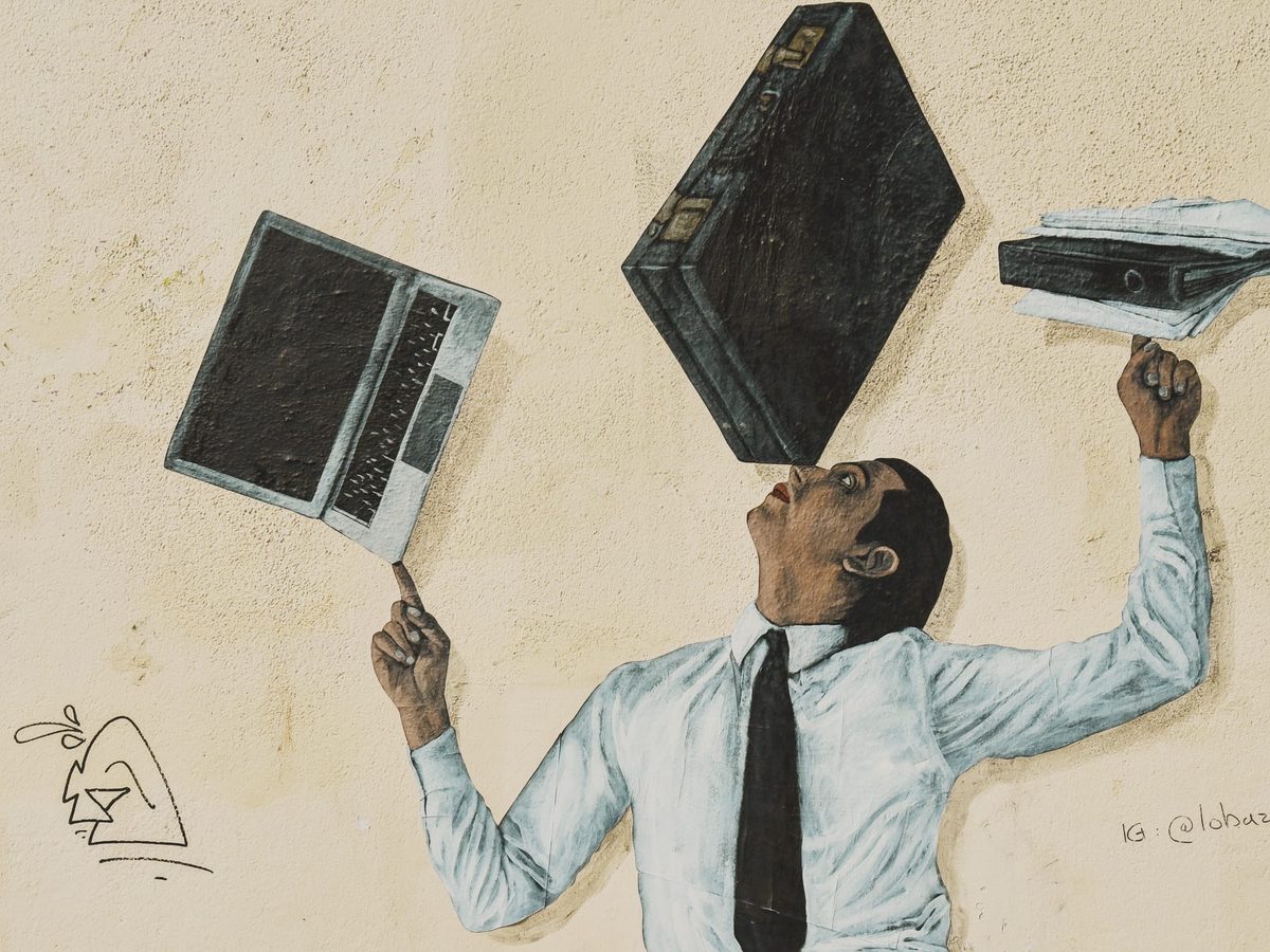 A mural of an office worker juggling a computer, a briefcase, and a stack of papers. Image Anthony Nelzin-Santos.