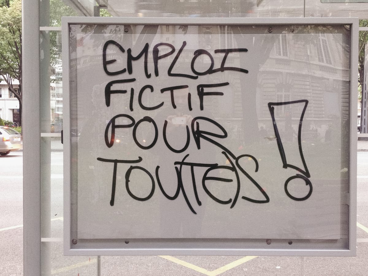 Un graffiti « Emploi fictif pour tou(te)s ! » sur un abribus.