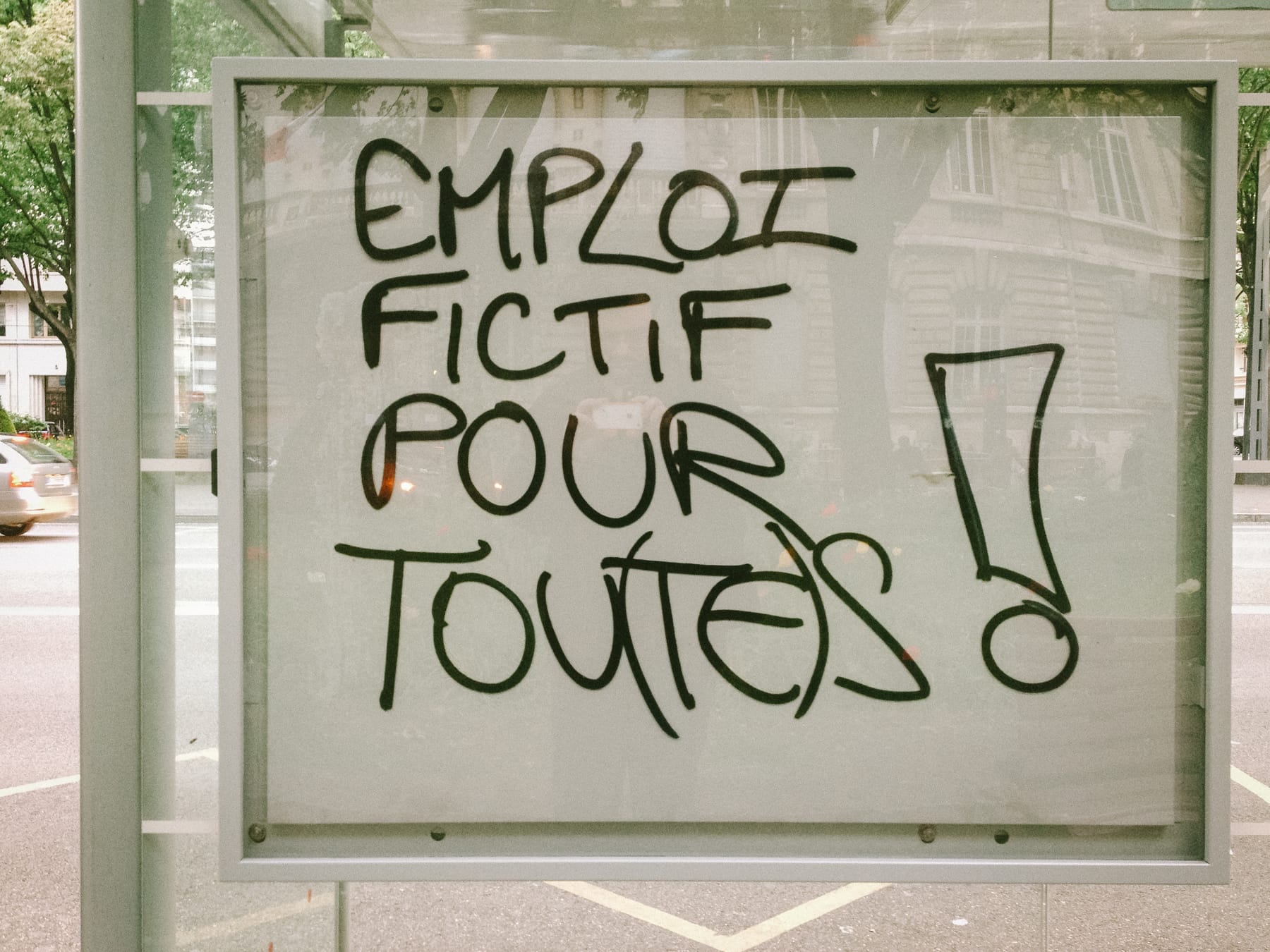 Un graffiti « Emploi fictif pour tou(te)s ! » sur un abribus.